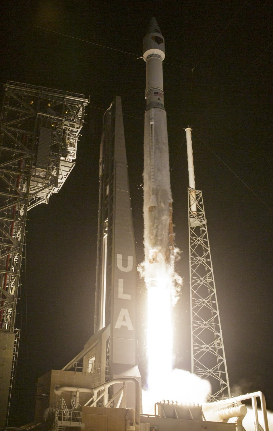 A rocket climbing into a clear sky on a bright pillar of flame, leaving a curving white exhaust trail
